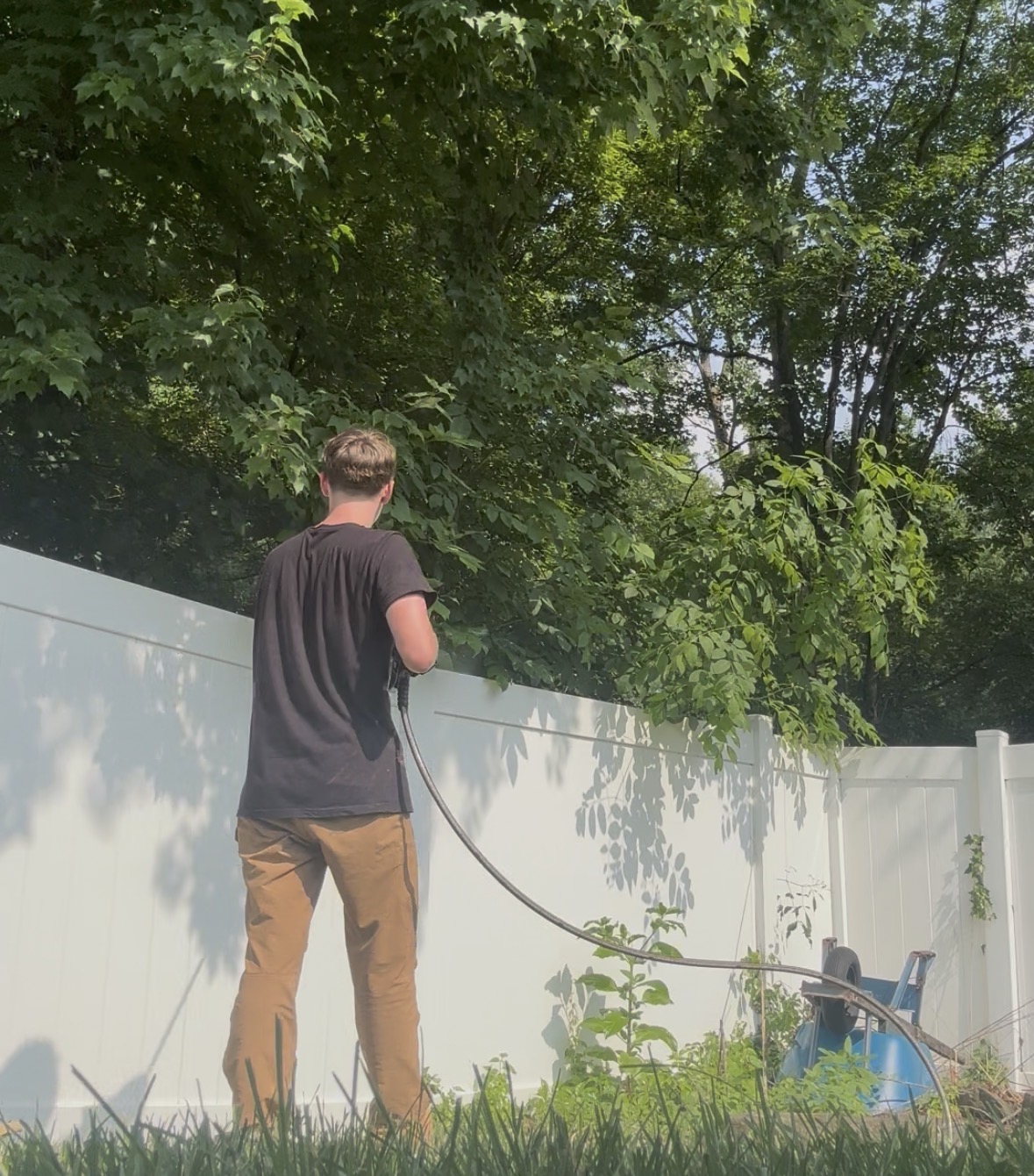 Technician power washing a white vinyl fence